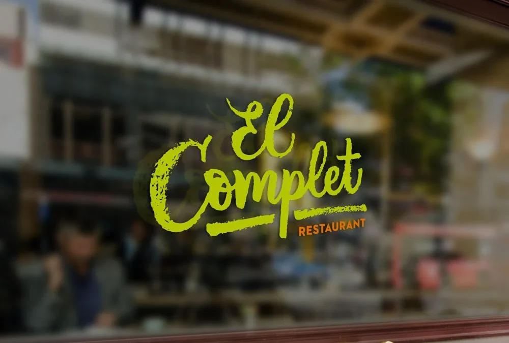 Logotipo de El Complet en lettering sobre un cristal, con el restaurante desenfocado al fondo