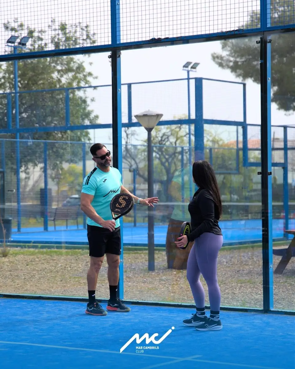 Entrenador de pádel dando indicaciones a una alumna en la pista